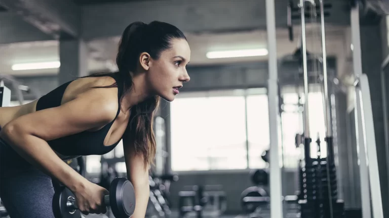 A imagem mostra uma mulher em uma academia levantando um haltere.