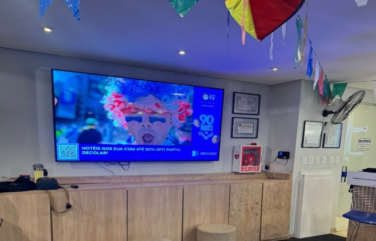 Tela horizontal instalada na recepção da Academia Via Campus exibindo conteúdo publicitário