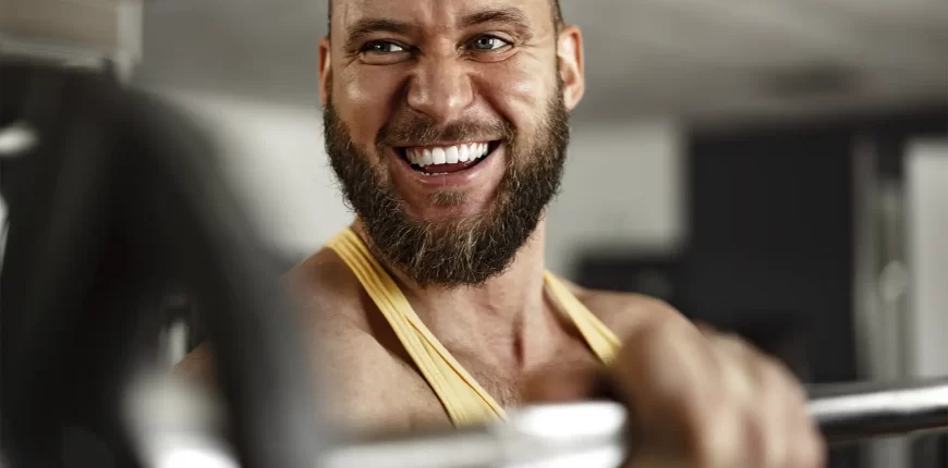 a imagem mostra um homem sorrindo levantando uma barra na academia